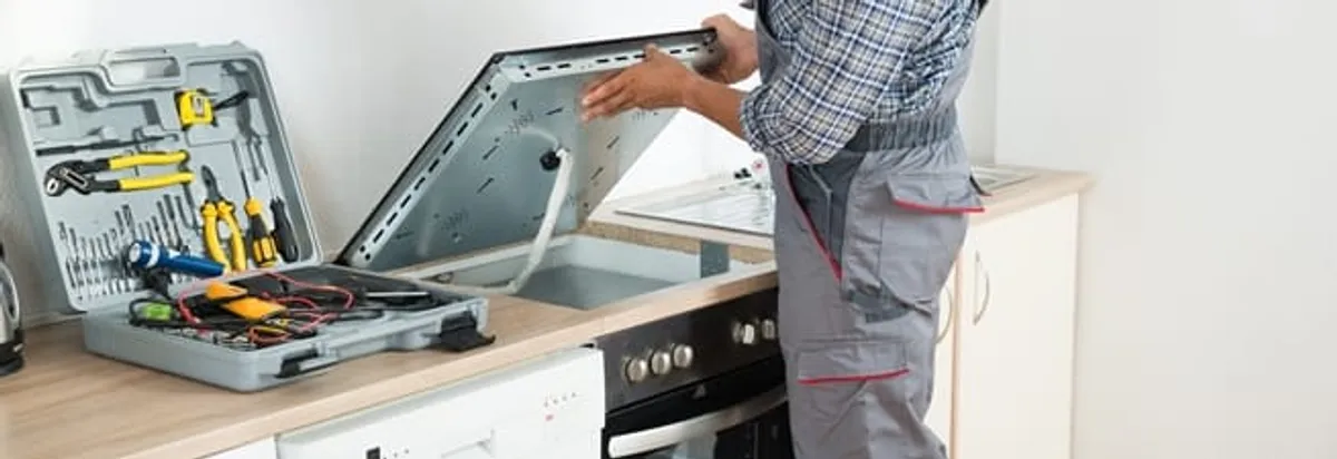 Cooktop repair technician lifting a built-in stovetop for service in Springfield, MO