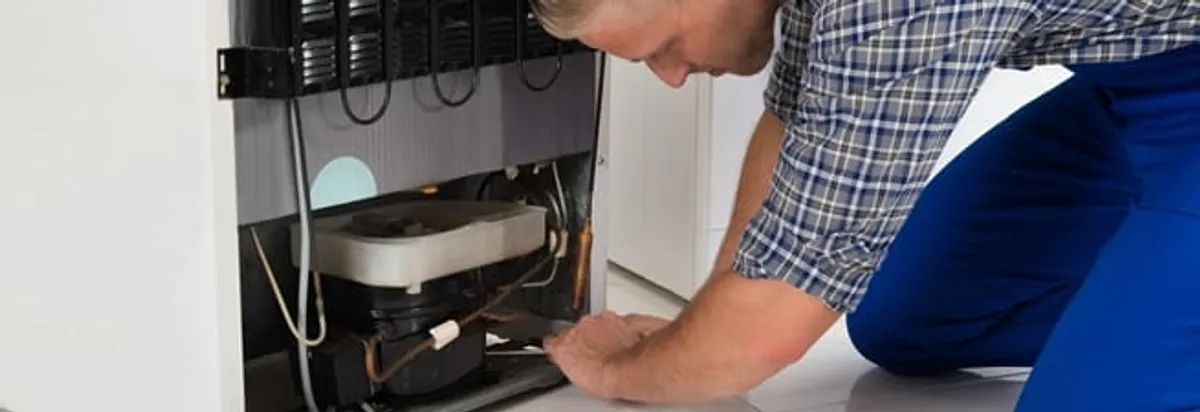 Refrigerator repair technician servicing the compressor and condenser area in Springfield, MO